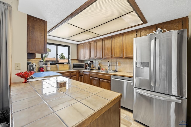 kitchen featuring backsplash, tile counters, sink, and stainless steel appliances