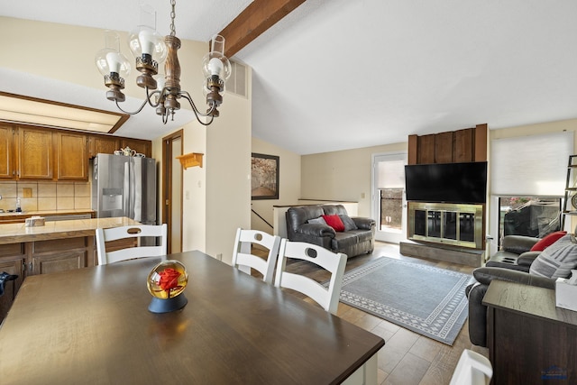 dining area with lofted ceiling with beams, a large fireplace, a chandelier, and light wood-type flooring