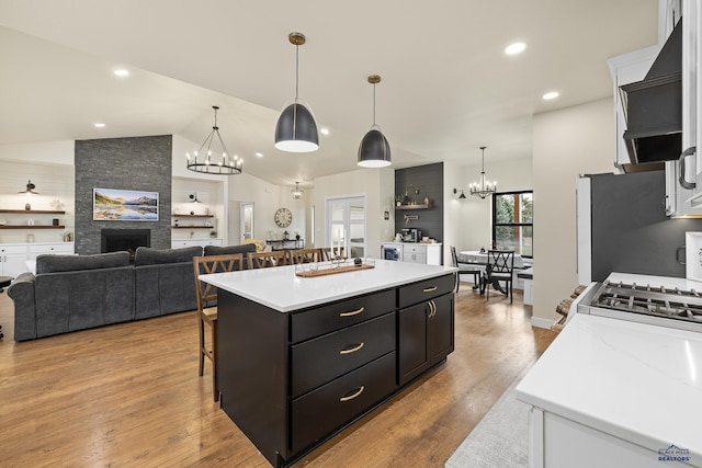 kitchen featuring decorative light fixtures, light hardwood / wood-style flooring, a fireplace, a kitchen island, and range hood