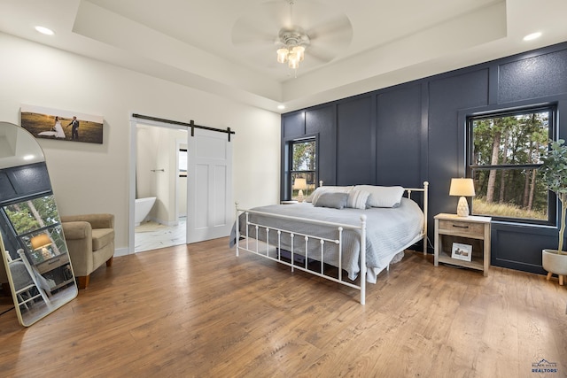 bedroom featuring wood-type flooring, a barn door, a raised ceiling, and ceiling fan