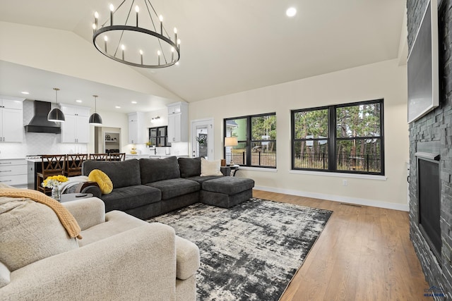 living room featuring a stone fireplace, light hardwood / wood-style flooring, high vaulted ceiling, and an inviting chandelier