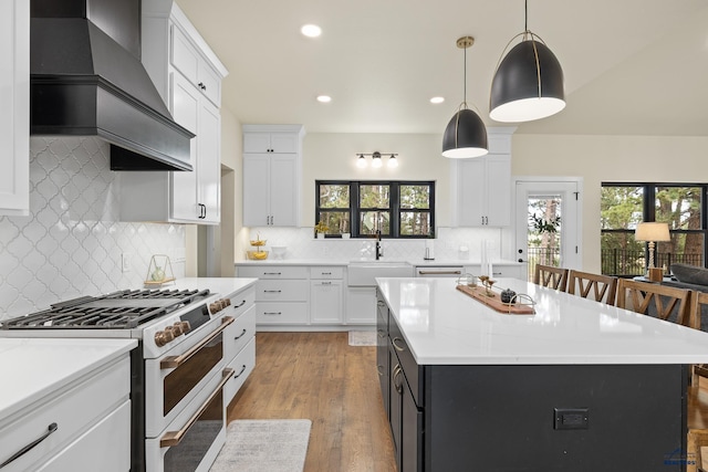 kitchen with high end range, custom range hood, hanging light fixtures, and an island with sink