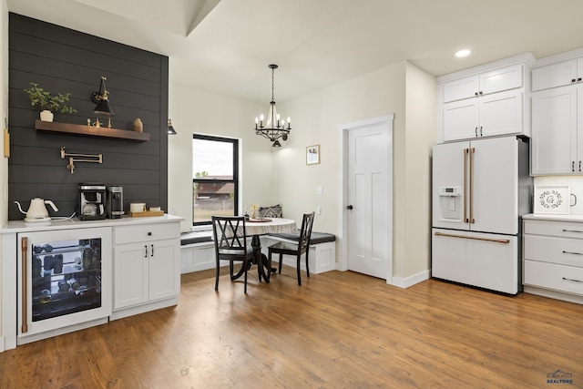 kitchen with hanging light fixtures, wine cooler, light hardwood / wood-style flooring, white refrigerator with ice dispenser, and white cabinets