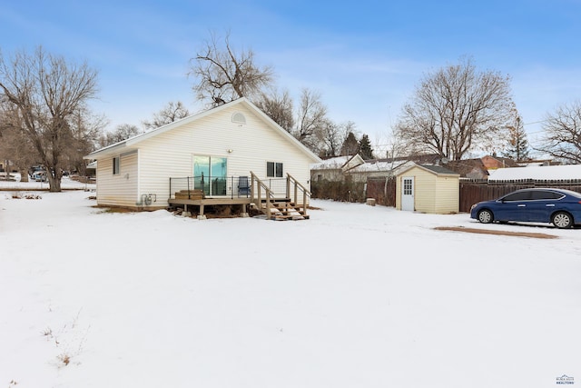 snow covered back of property featuring a deck and a storage unit