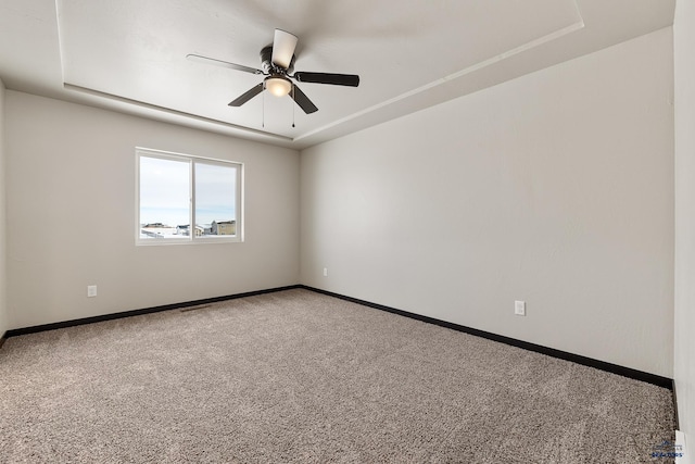 empty room featuring carpet, ceiling fan, and a raised ceiling