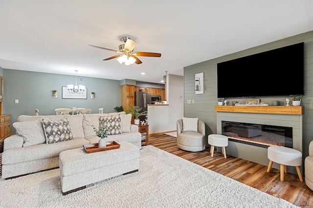 living room with wood walls, a fireplace, ceiling fan with notable chandelier, and hardwood / wood-style flooring