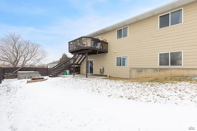 snow covered house with a hot tub and a wooden deck