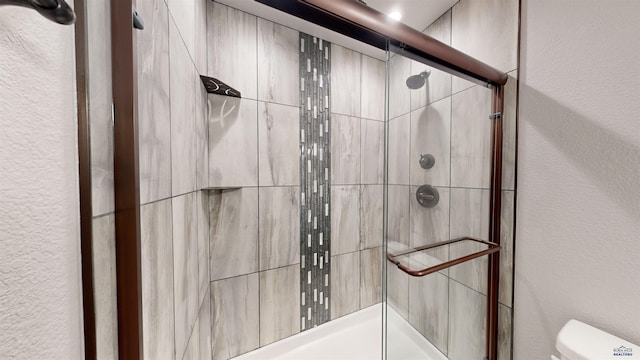 bathroom featuring a shower with door and toilet