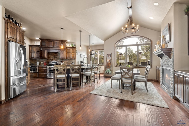 dining room featuring vaulted ceiling, dark hardwood / wood-style floors, sink, a stone fireplace, and a chandelier