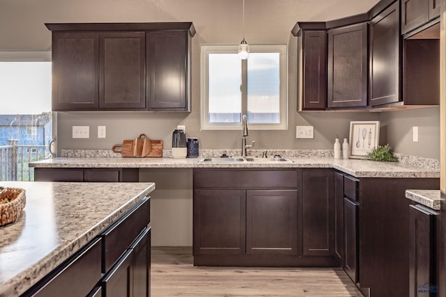 kitchen with decorative light fixtures, light hardwood / wood-style floors, sink, dark brown cabinetry, and light stone counters