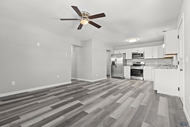 kitchen with wood-type flooring, sink, light stone countertops, stainless steel appliances, and white cabinets