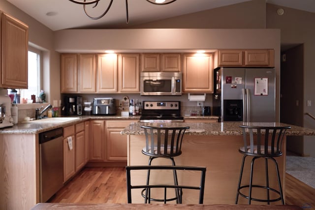 kitchen with appliances with stainless steel finishes, a center island, light brown cabinetry, sink, and vaulted ceiling