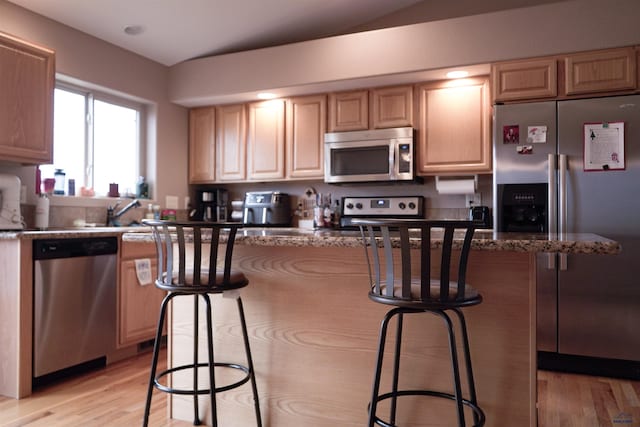 kitchen with light brown cabinetry, appliances with stainless steel finishes, and dark stone counters