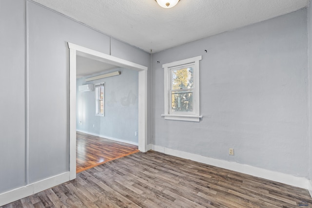 empty room with hardwood / wood-style flooring, a textured ceiling, and a wall unit AC