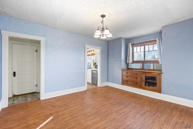 unfurnished living room featuring hardwood / wood-style flooring, a wealth of natural light, a textured ceiling, and a notable chandelier