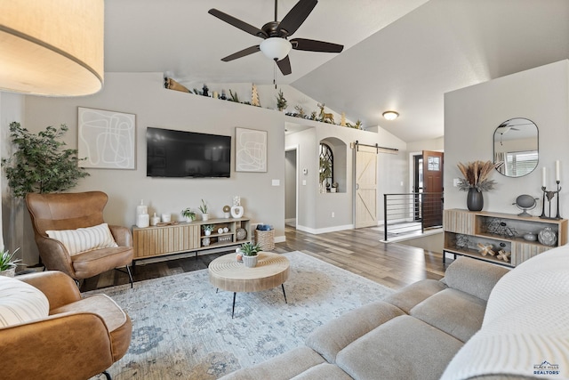 living room featuring ceiling fan, hardwood / wood-style floors, a barn door, and vaulted ceiling