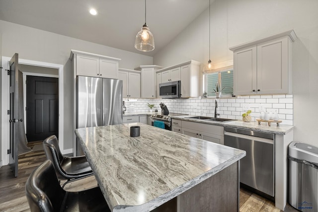 kitchen featuring stainless steel appliances, hanging light fixtures, vaulted ceiling, a kitchen island, and sink