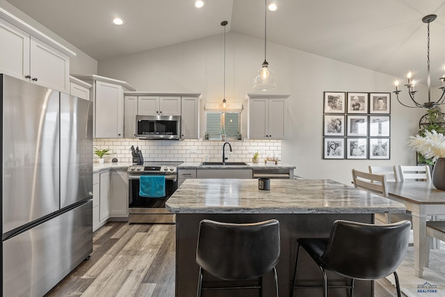 kitchen featuring pendant lighting, a kitchen island, stainless steel appliances, backsplash, and light stone counters