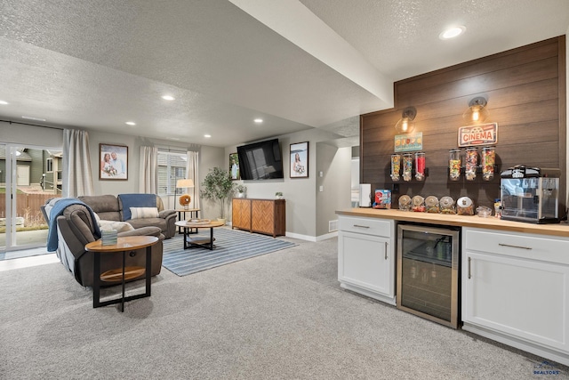 bar with a textured ceiling, light carpet, beverage cooler, and white cabinets