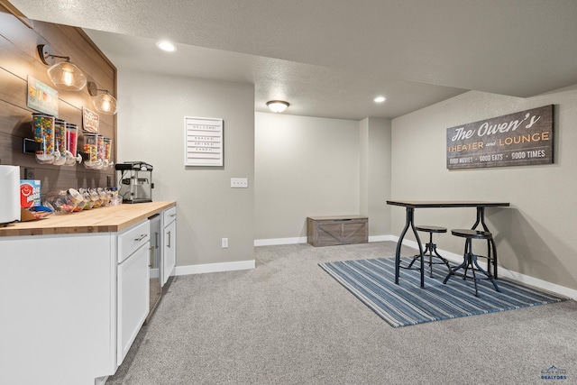 bar featuring a textured ceiling, wood counters, carpet, and white cabinets