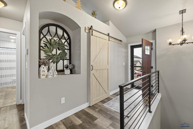 foyer entrance featuring an inviting chandelier, lofted ceiling, a barn door, and dark hardwood / wood-style floors