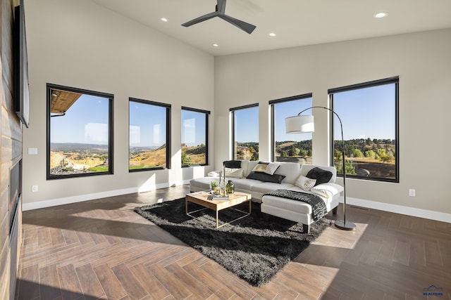 living room featuring ceiling fan, plenty of natural light, dark parquet flooring, and a towering ceiling