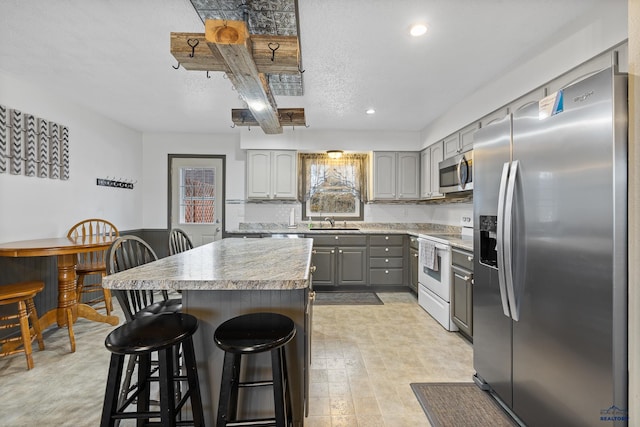 kitchen with appliances with stainless steel finishes, gray cabinetry, a kitchen bar, and a center island