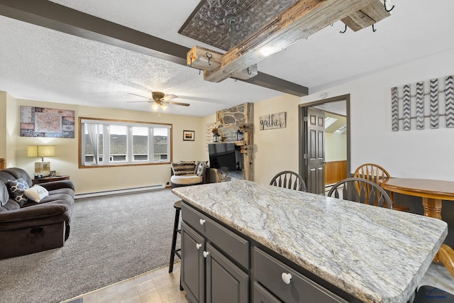 kitchen featuring light carpet, ceiling fan, baseboard heating, light stone countertops, and a center island