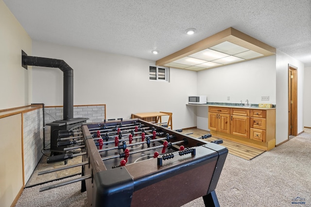 recreation room featuring light colored carpet, a wood stove, and a textured ceiling