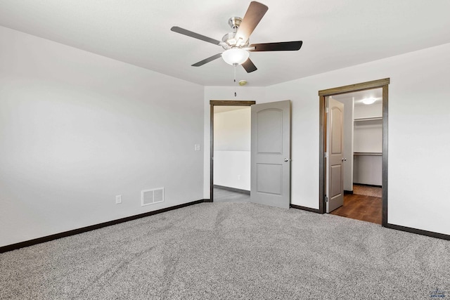 unfurnished bedroom featuring ceiling fan, a closet, a spacious closet, and dark carpet