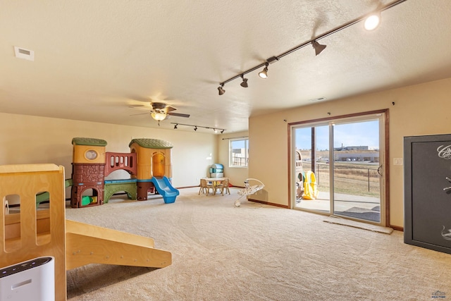 game room featuring rail lighting, light carpet, ceiling fan, and a textured ceiling