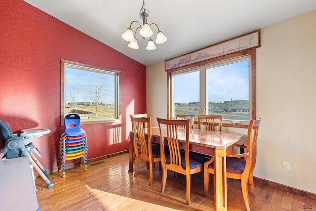 dining room featuring an inviting chandelier, vaulted ceiling, and light wood-type flooring