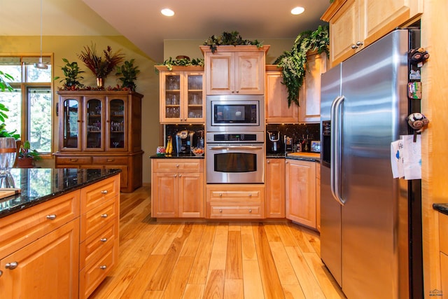 kitchen featuring light hardwood / wood-style floors, stainless steel appliances, and dark stone counters