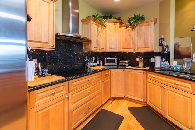 kitchen with dark stone counters, wall chimney range hood, sink, backsplash, and stainless steel appliances