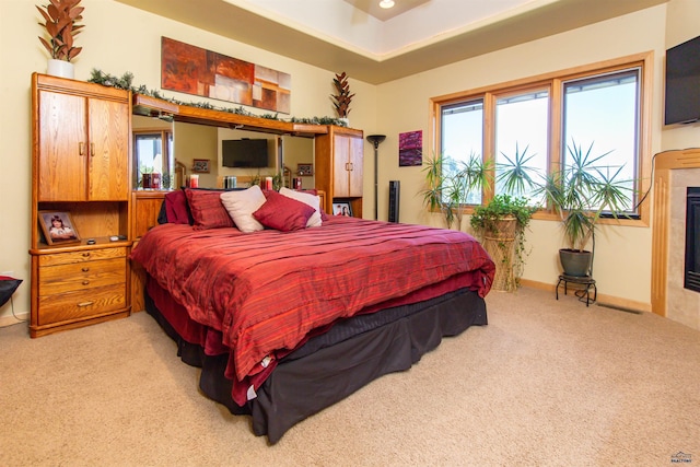 bedroom featuring a tiled fireplace, light colored carpet, and multiple windows