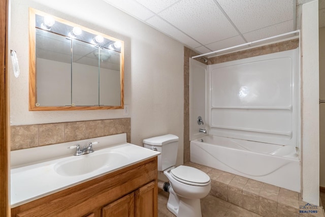 full bathroom featuring tub / shower combination, a drop ceiling, toilet, and vanity