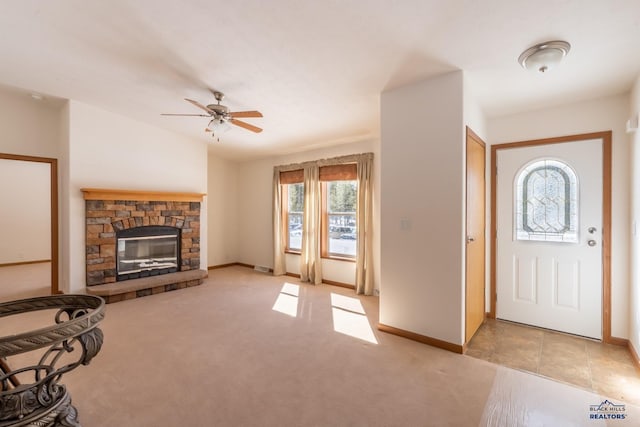 foyer entrance with ceiling fan, light carpet, and a fireplace