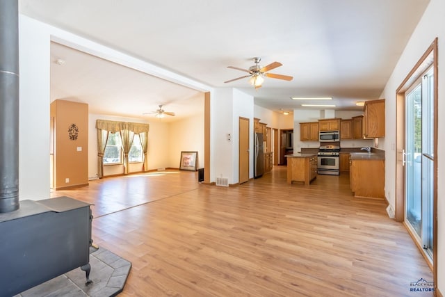 living room featuring ceiling fan, a wood stove, vaulted ceiling with beams, and light wood-type flooring