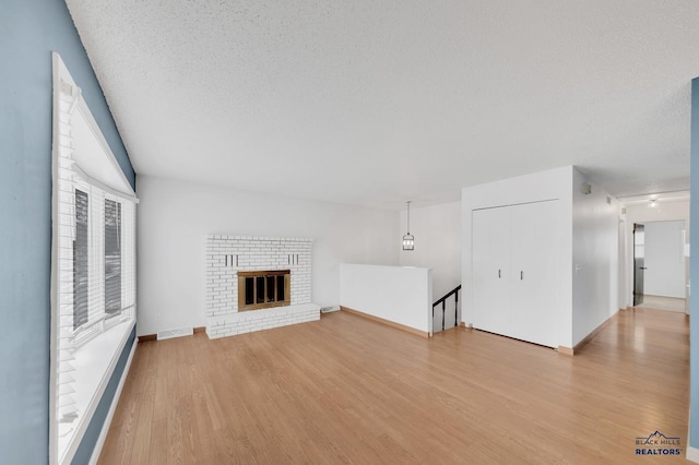 unfurnished living room featuring light wood-type flooring, a wealth of natural light, a brick fireplace, and a textured ceiling