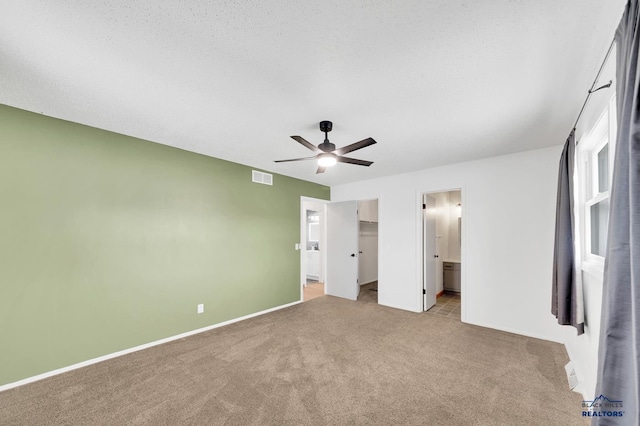 unfurnished bedroom featuring ceiling fan, light colored carpet, connected bathroom, and a textured ceiling