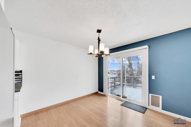 empty room with light hardwood / wood-style floors, a textured ceiling, and an inviting chandelier