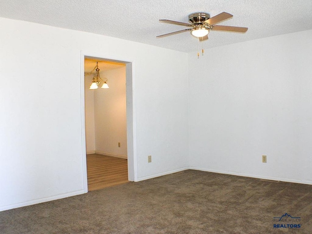 spare room featuring ceiling fan with notable chandelier, dark colored carpet, and a textured ceiling