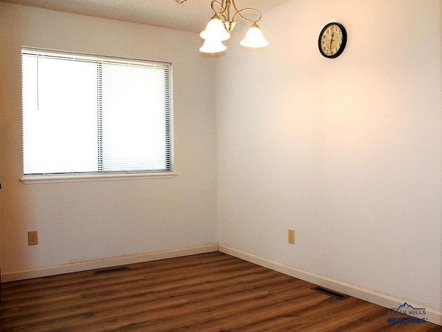 empty room featuring a wealth of natural light, dark hardwood / wood-style floors, and a notable chandelier