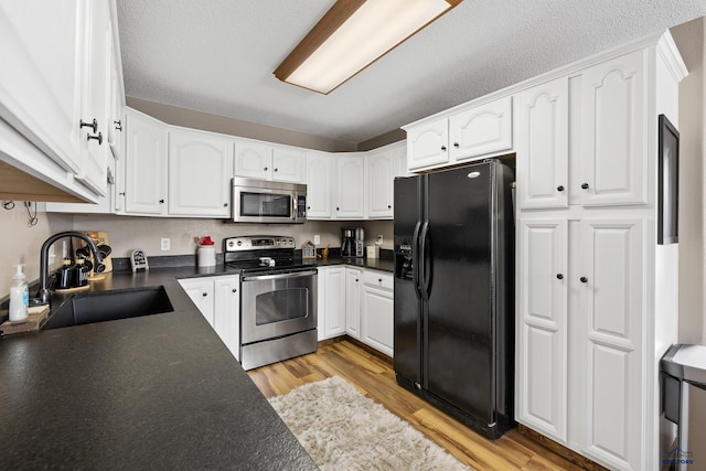 kitchen with a textured ceiling, white cabinets, appliances with stainless steel finishes, sink, and light wood-type flooring