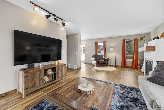 living room featuring wood-type flooring, a brick fireplace, and track lighting