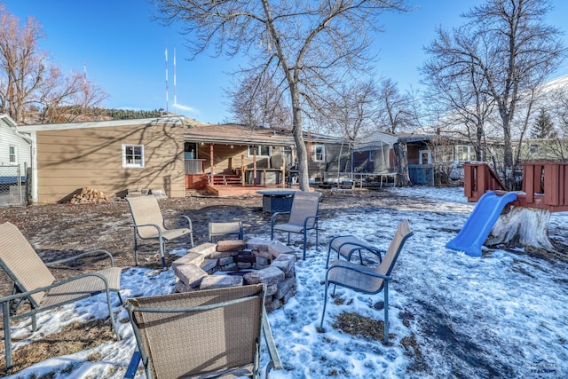 snow covered back of property with a playground, a trampoline, and a fire pit