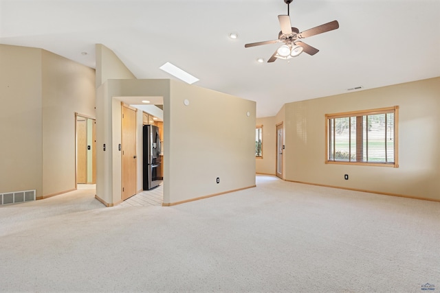 carpeted spare room featuring lofted ceiling with skylight and ceiling fan