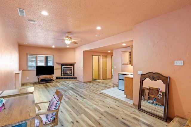 living room featuring ceiling fan, light hardwood / wood-style floors, a tile fireplace, and a textured ceiling