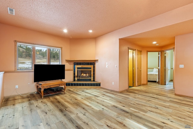 living room with a tiled fireplace, light hardwood / wood-style flooring, and a textured ceiling