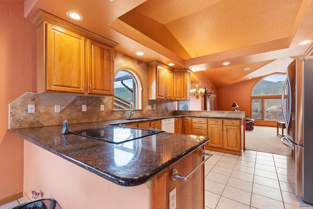 kitchen featuring lofted ceiling, dark stone countertops, stainless steel refrigerator, kitchen peninsula, and dishwasher